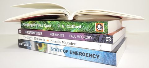 An open paperback on a stack of customers' paperbacks, spines showing the variety of sizes and covers