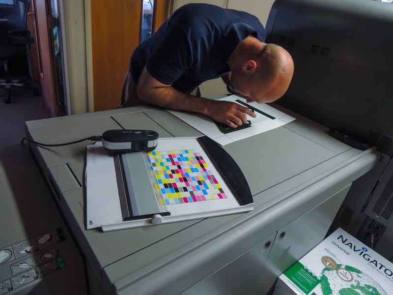 An operator checking a colour calibration chart at a colour press, a spectrophotometer on the chart holder