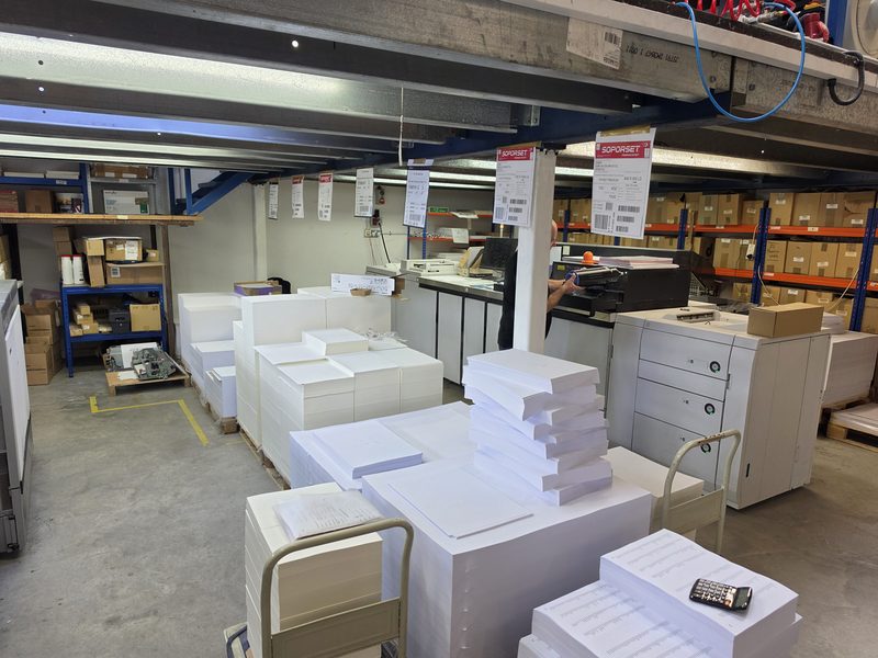 Stacks of printed sheets and paper beside the presses in the press room