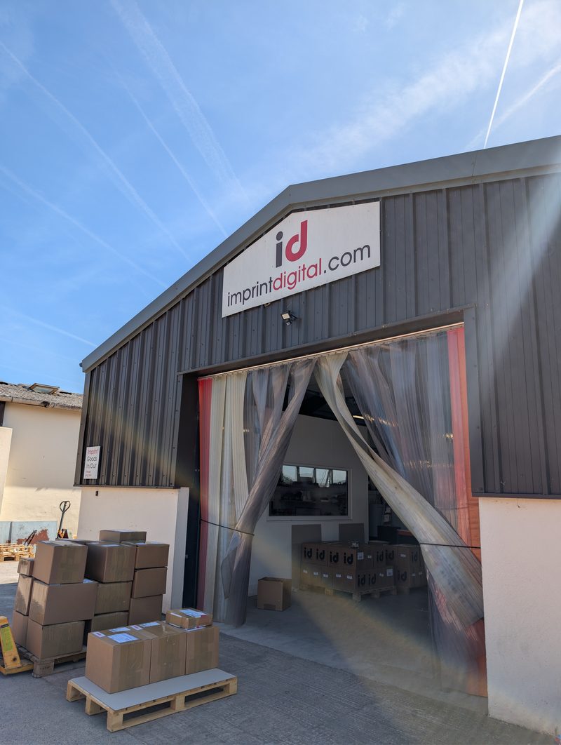 Our works near Exeter: the grey-clad building with the imprintdigital.com sign, its door open, cartons on pallets outside